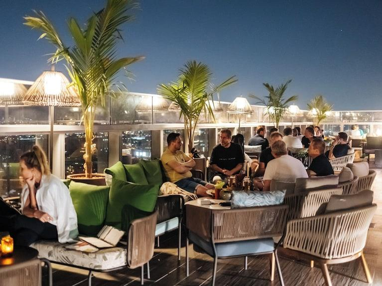 Guests on the rooftop lounge at night with palms and city views